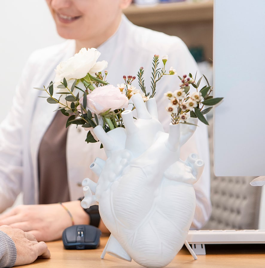 weiße Vase in Form eines anatomischen Herzens, mit Blumen